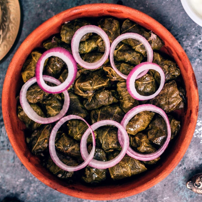 Close-up of a terracotta bowl filled with dolmades, garnished with red onion rings.