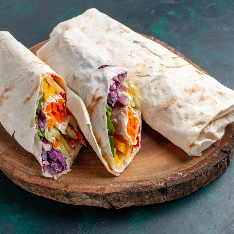 Three colorful vegetable wraps, two open and one closed, on a rustic wooden board.