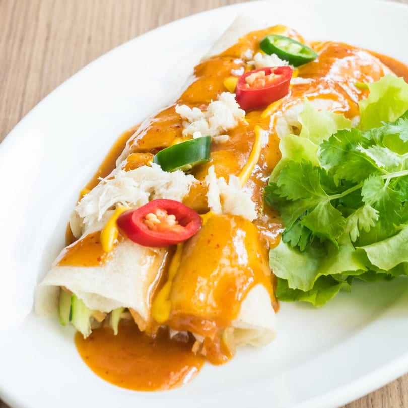 Spring rolls drizzled with orange sauce, topped with crab meat, chili, and a side of lettuce.