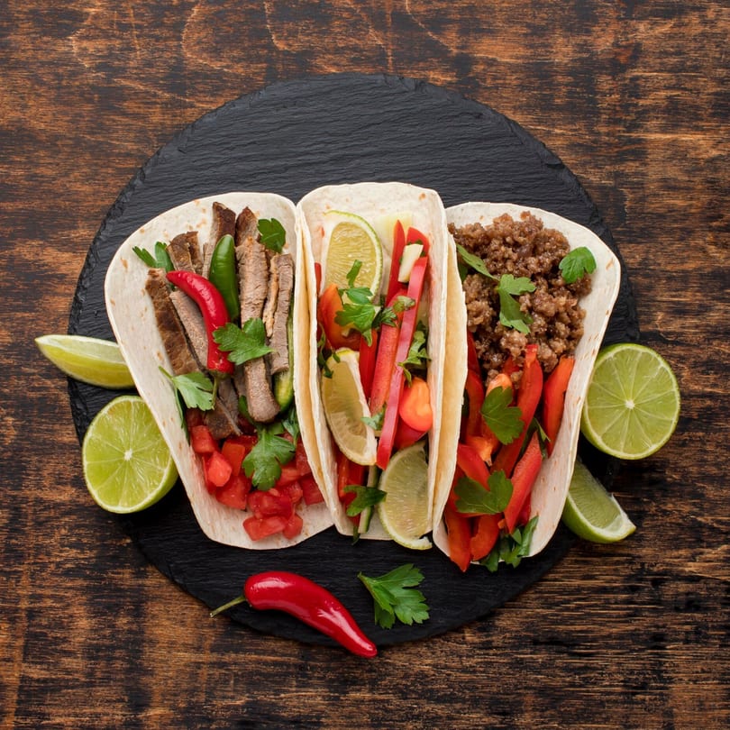 Three tacos, one with steak, one with vegetables, and one with ground beef, on a dark wooden table.
